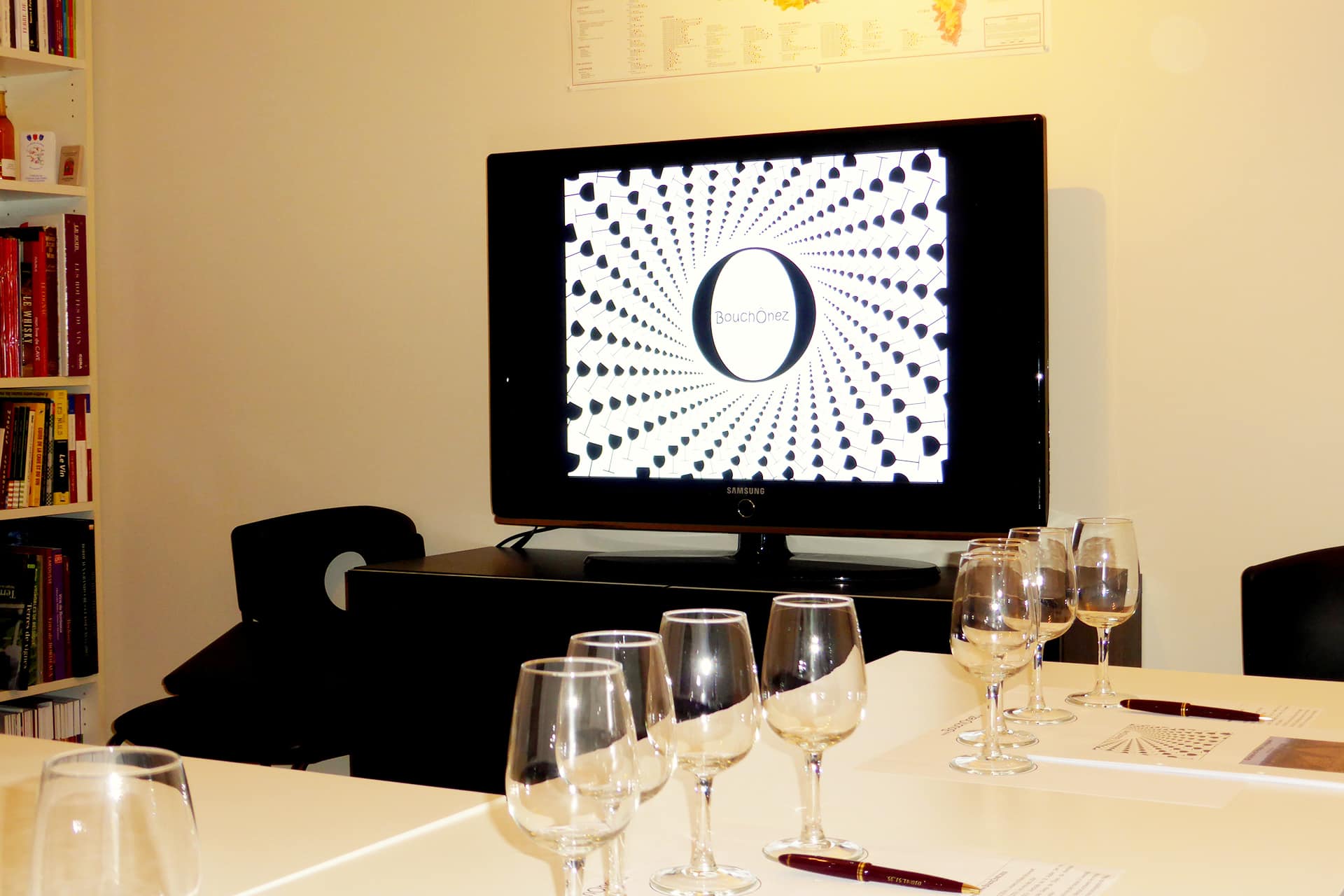 Télévision avec le logo Bouchonez ainsi qu'une table avec des verres à vin